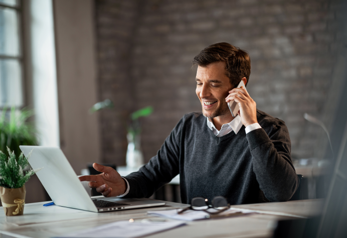 man smiling and talking on phone while sitting at desk