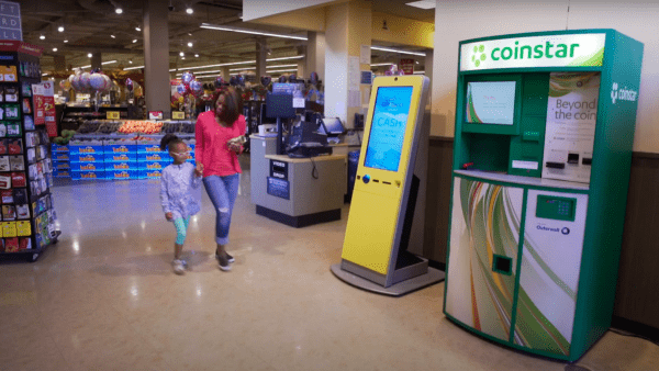 an adult and child walking passed a coinstar machine