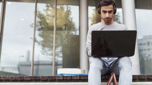 Young man with headphones working on his computer and sitting outdoors