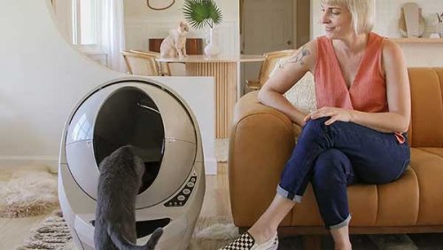 Woman in the couch looking at the cat going inside the litter robot